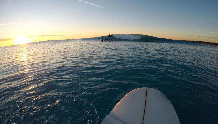 Surfista iniciante praticando a remada em uma prancha de surf, preparando-se para pegar a primeira onda, simbolizando o aprendizado das técnicas básicas de surf.